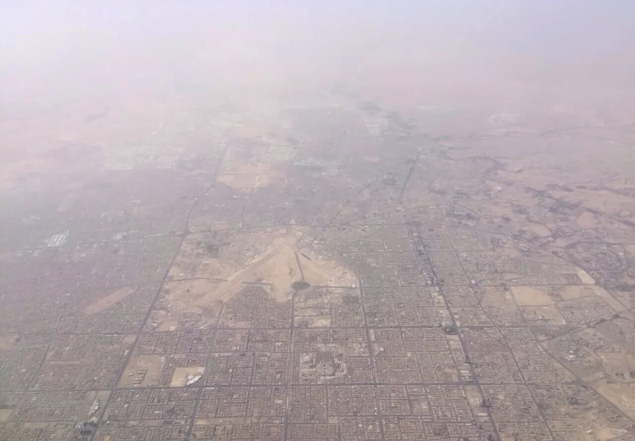 Aerial view of King Khalid International Airport showing several terminal buildings, parallel runways, and arid land around Riyadh.