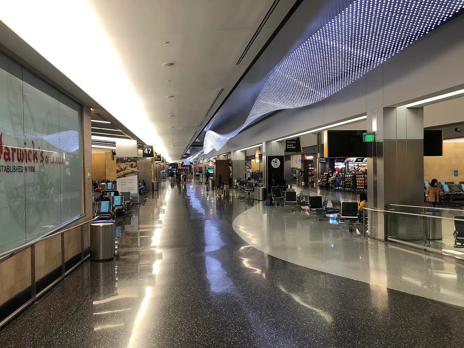 A long, brightly lit passenger corridor inside Terminal 2 with gate signage, seating areas, and moving walkways.