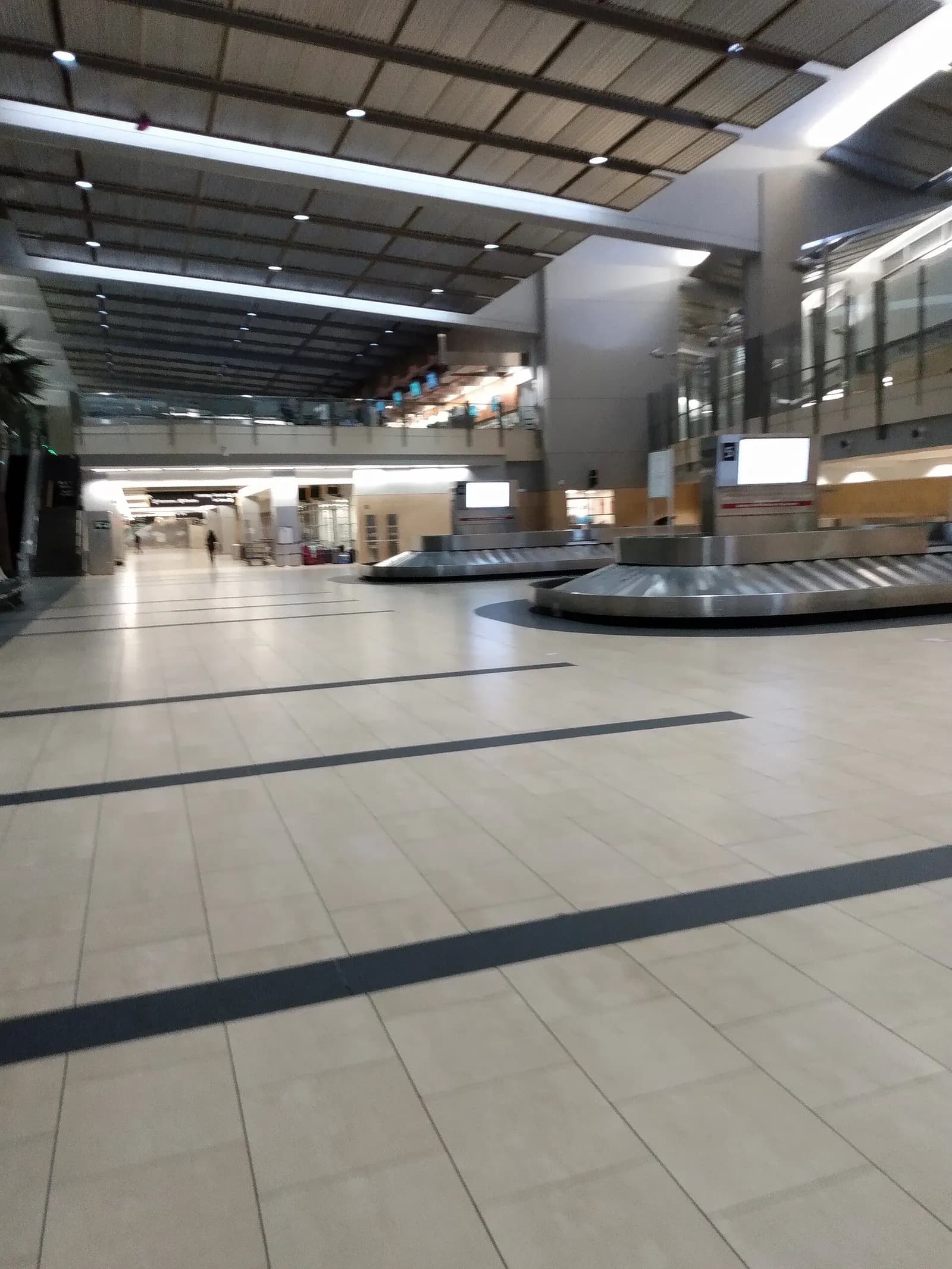 The baggage claim hall at San Diego International Airport with multiple carousels, tiled floors, and overhead flight information displays.