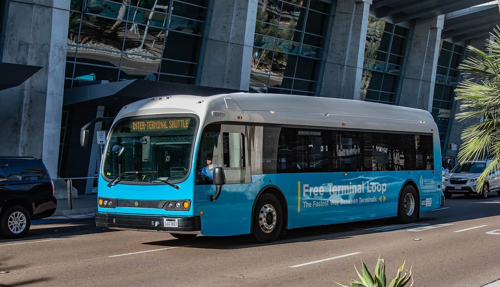 A green electric Proterra shuttle bus labeled for SAN airport service parked outside Terminal 2.