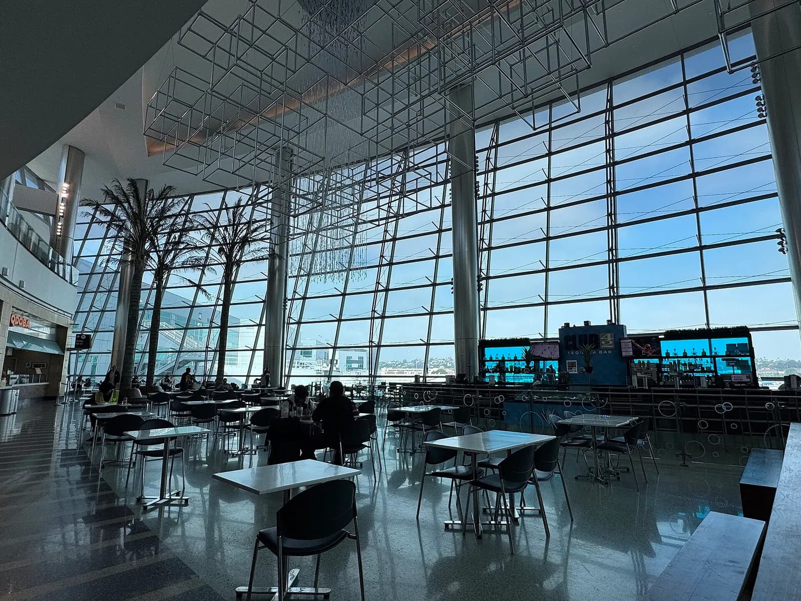 The glass-fronted Terminal 2 building at San Diego International Airport on a sunny day, with palm trees and passenger drop-off lanes in the foreground.