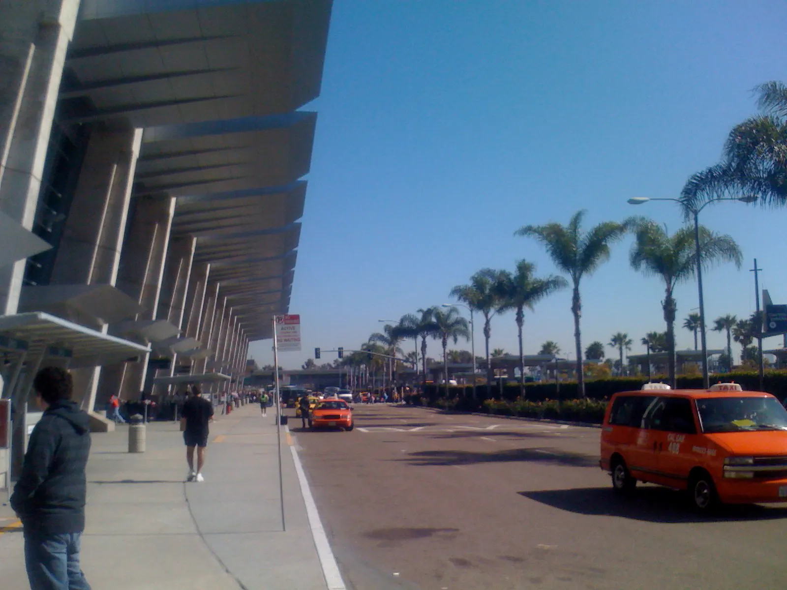 The exterior sidewalk and entrance area outside Terminal 2, showing the terminal building facade and landscaping.