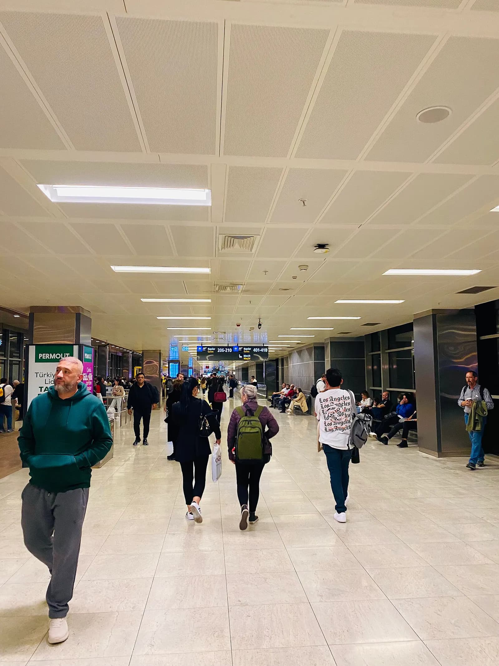 A long domestic departures corridor with tiled floors, ceiling lights, and passengers walking toward the gates.