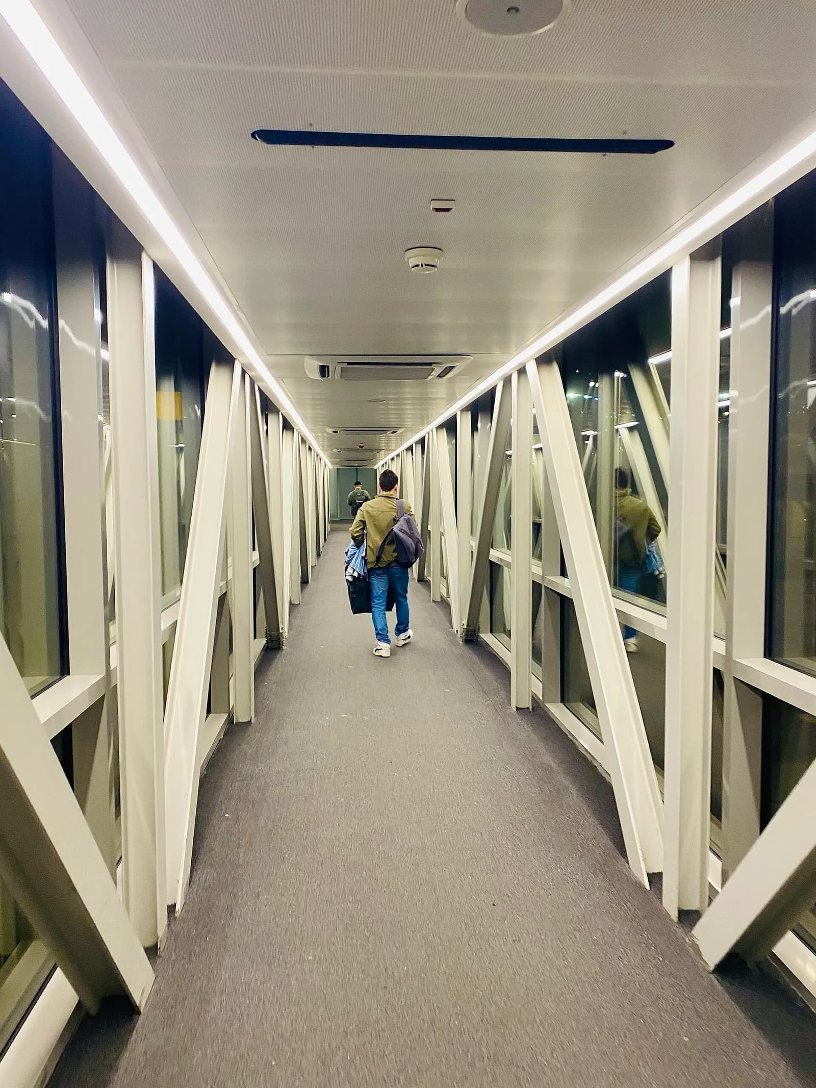 Passengers walking down a covered jet bridge from gate 212 to board an aircraft on the apron.