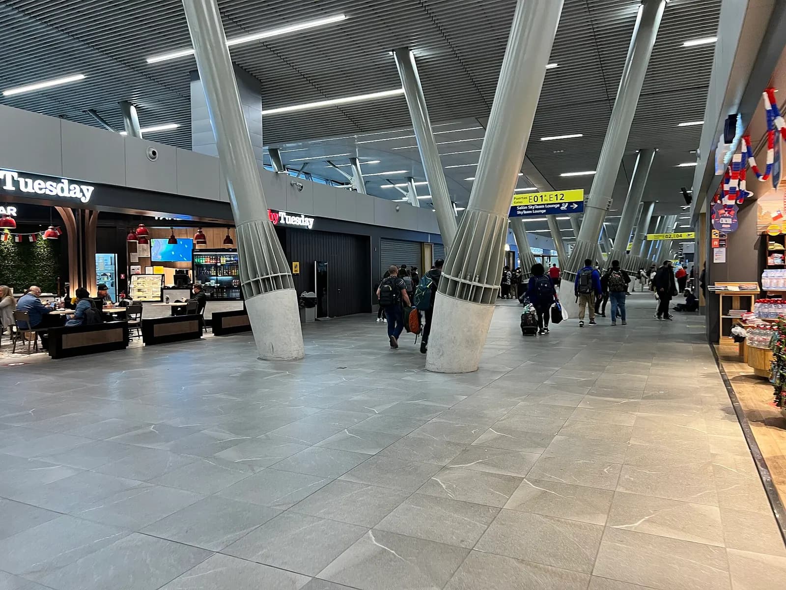 A long indoor corridor in the international terminal with shops, seating, and passengers walking toward the gates.