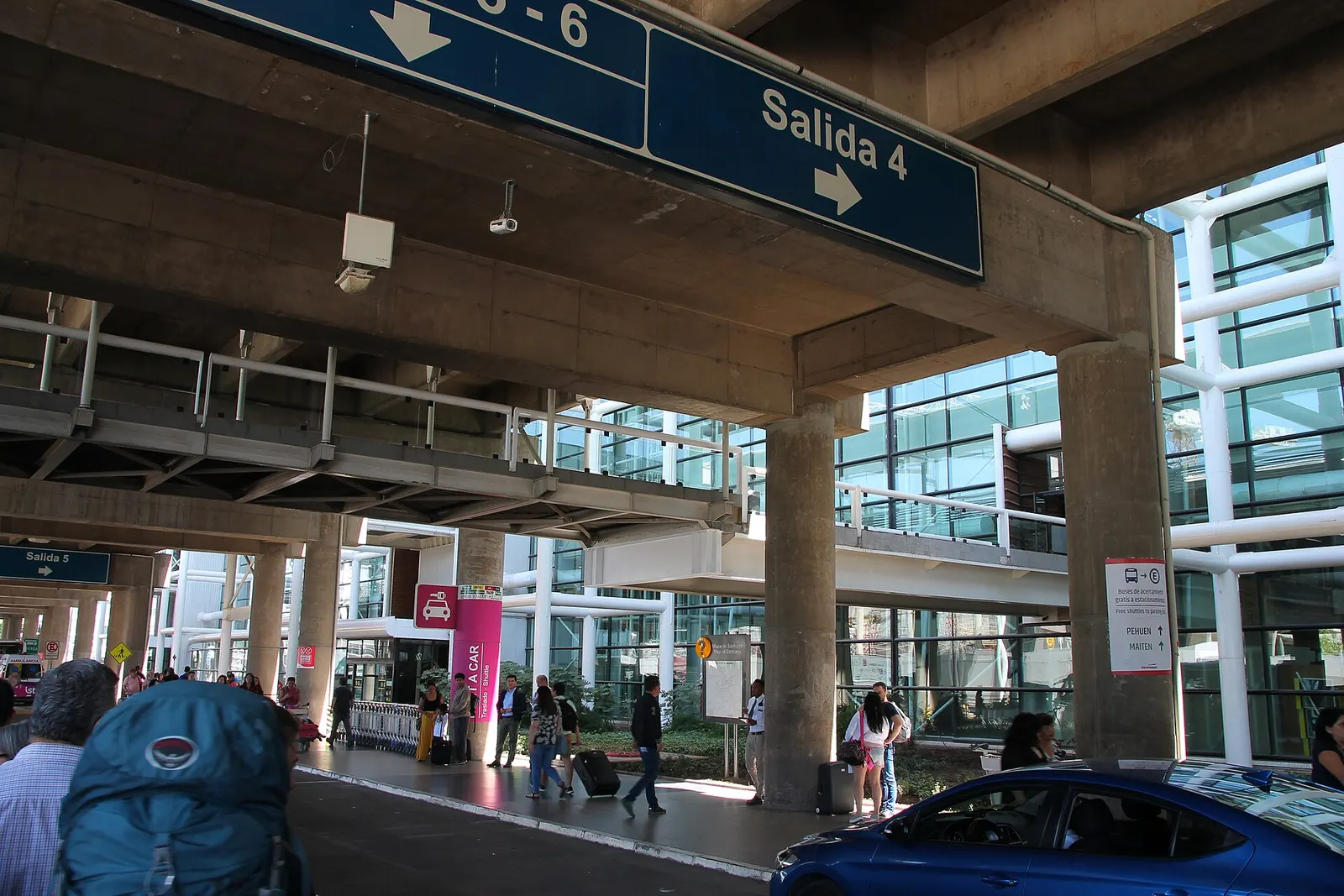 Airport shuttle buses at marked stops outside the terminal building with Spanish-language signs.