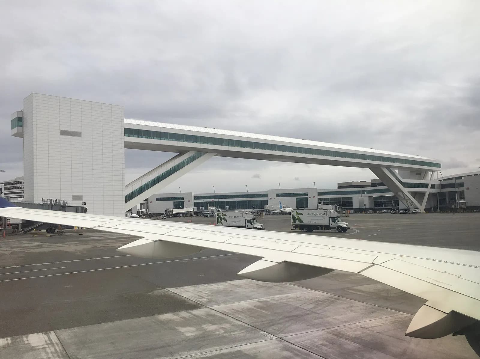 An enclosed pedestrian walkway with glass walls connecting sections of the airport terminal complex.