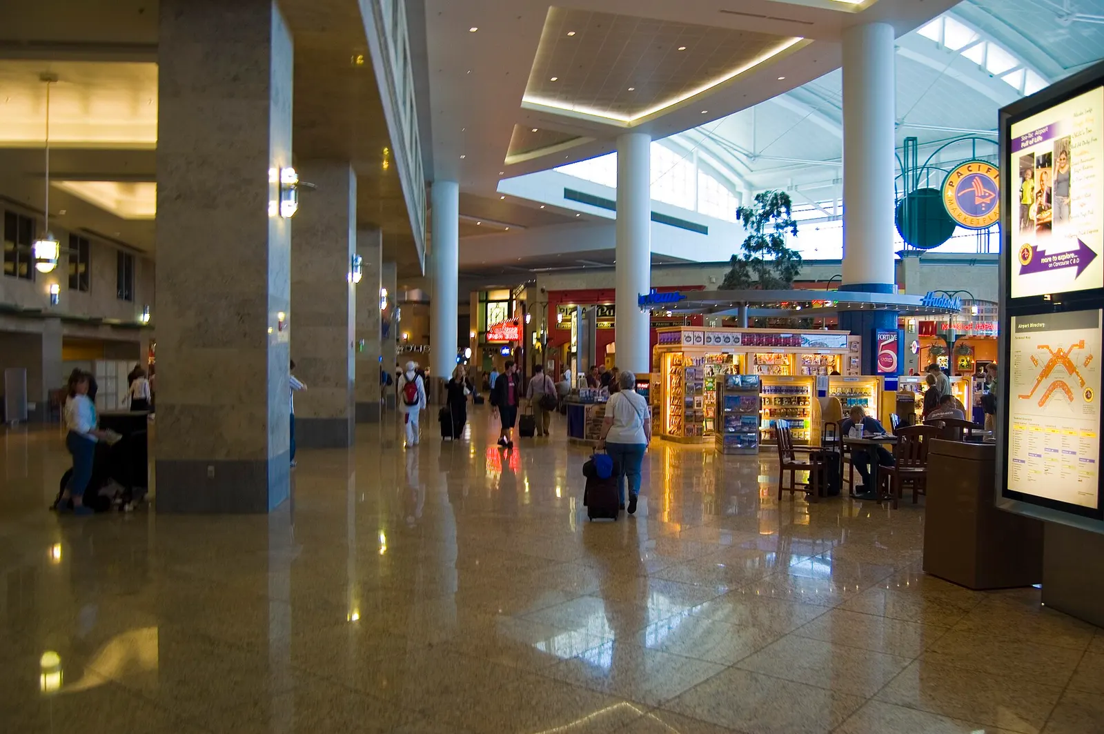 The airport's central food court and shopping area with restaurant counters, retail storefronts, and seated travelers.