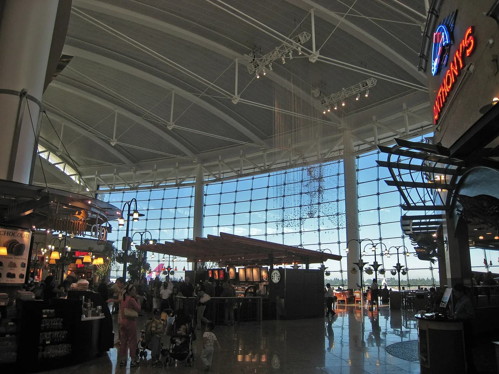 A wide interior view of the bustling main terminal concourse with high ceilings, signage, and travelers moving through the space.