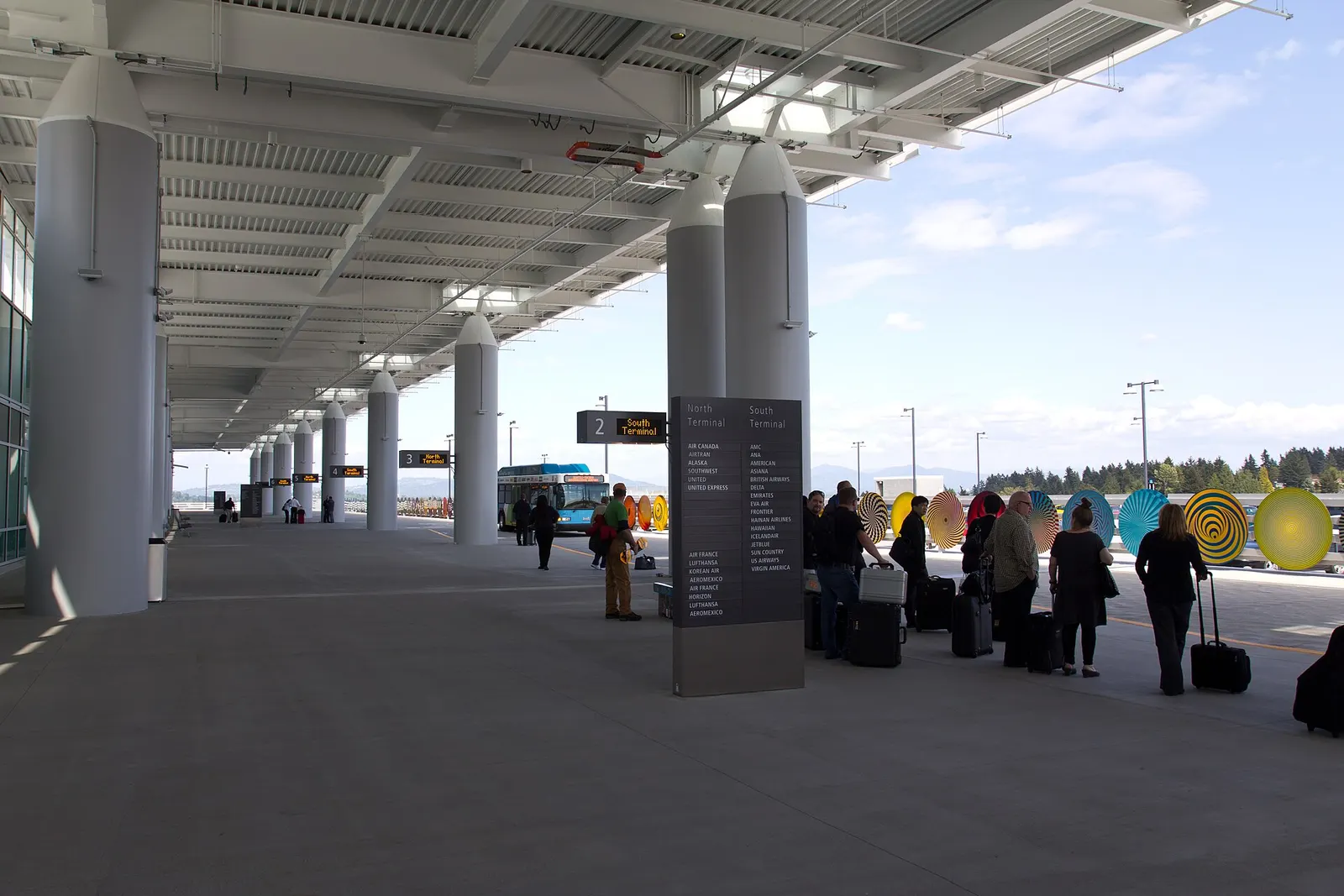 Color-coded bay signs mark shuttle pickup stops along the airport arrivals roadway.