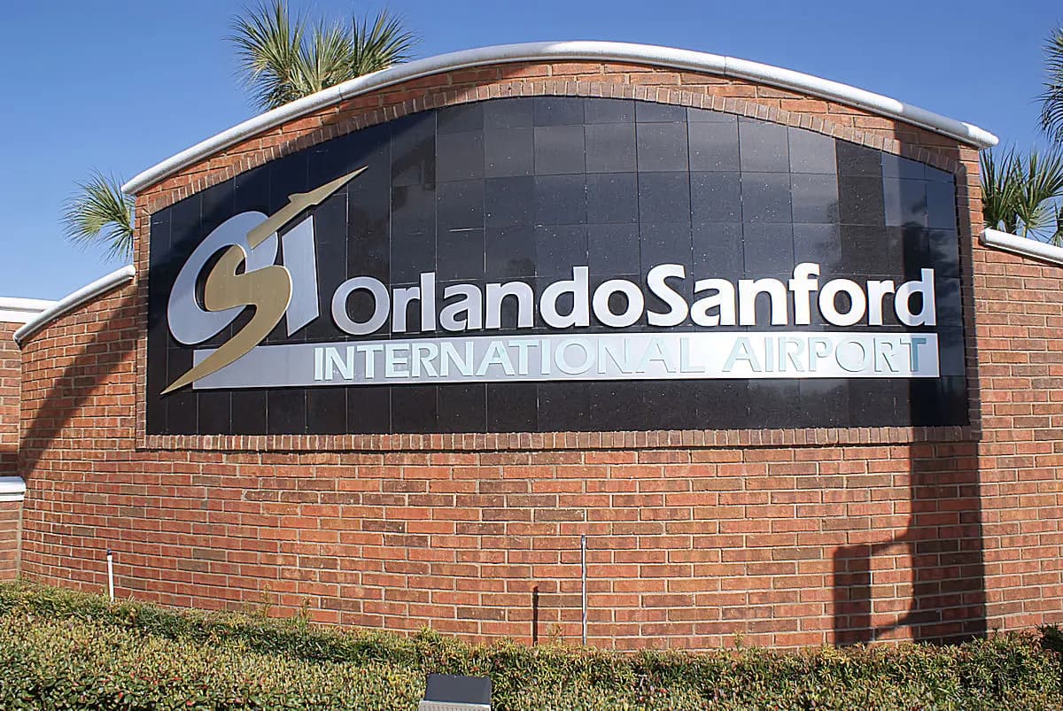 Roadside Orlando Sanford International Airport sign with palm trees and a clear Florida sky.