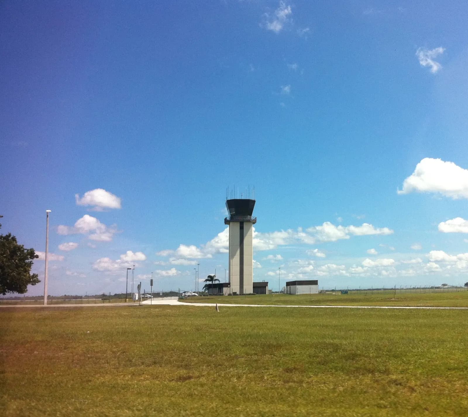 Orlando Sanford International Airport control tower rising above trees under a blue sky.
