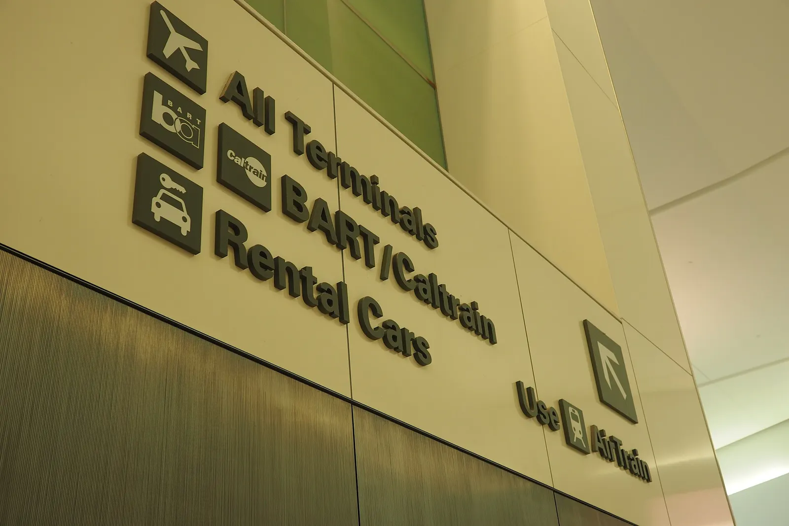 Overhead wayfinding signs in a terminal corridor point travelers toward AirTrain, domestic terminals, and international gates.