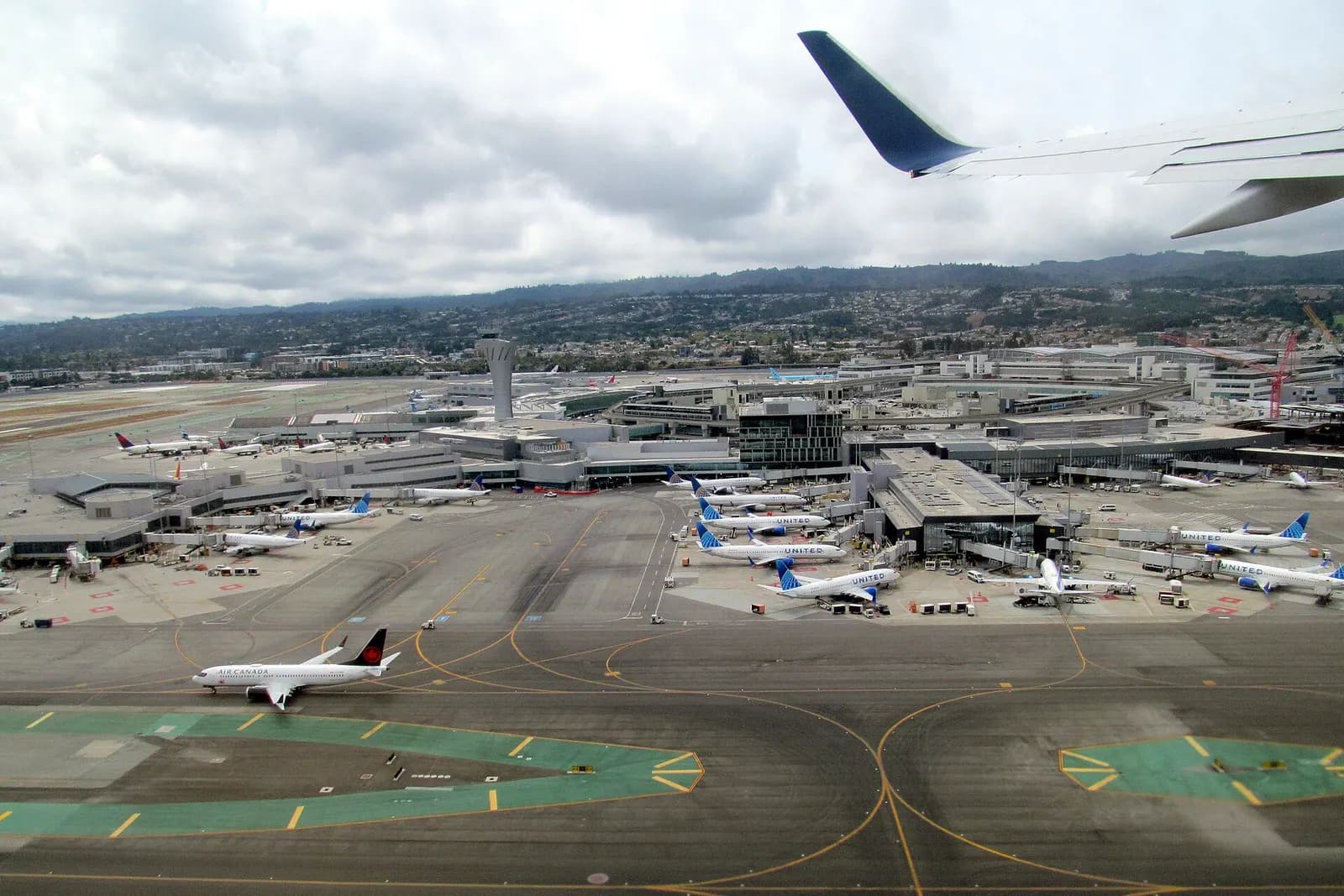 An aerial view from a departing flight shows SFO's parallel runways, terminals, and cargo areas along the San Francisco Bay shoreline.