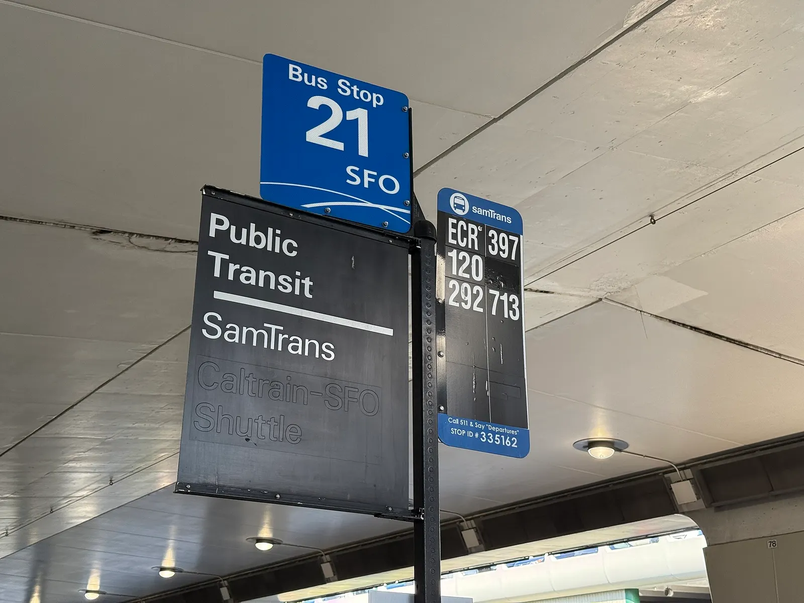A SamTrans public bus stop with route signage on the curb outside San Francisco International Airport.