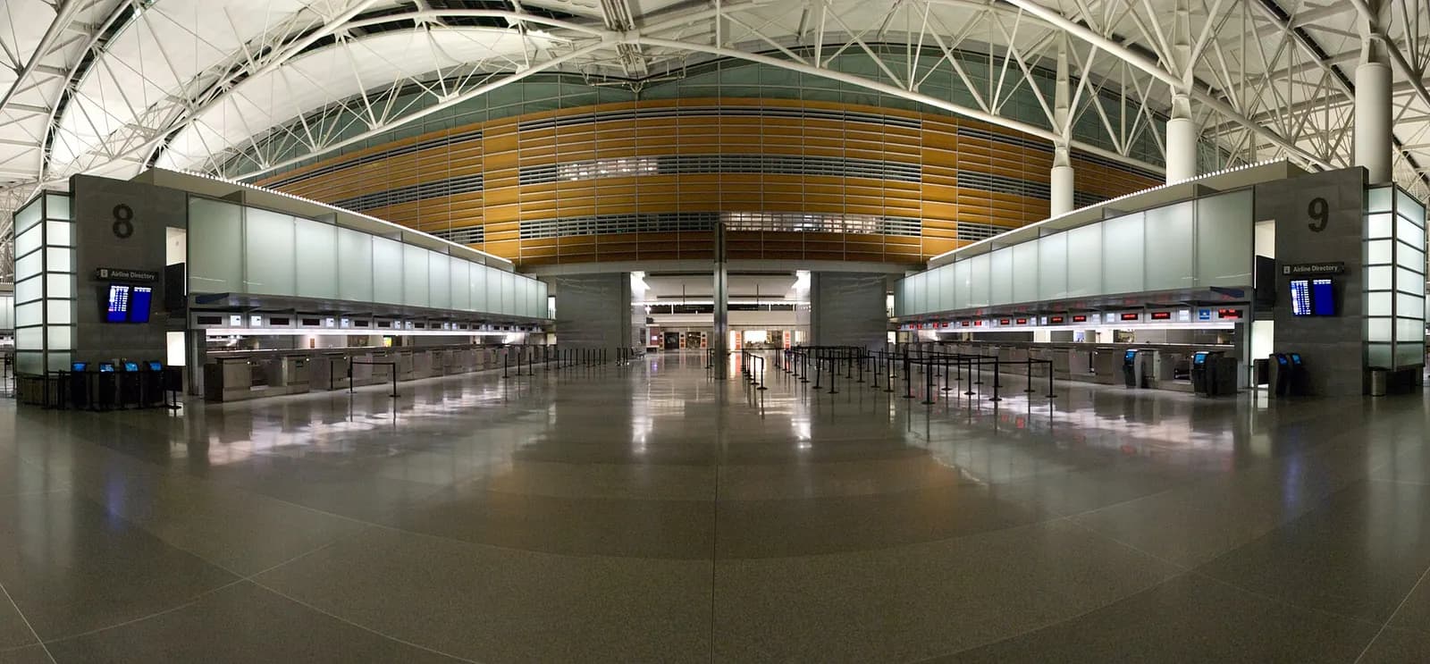 A wide panoramic view of the bright, modern interior of SFO's International Terminal with high ceilings, gate areas, and travelers moving through the concourse.