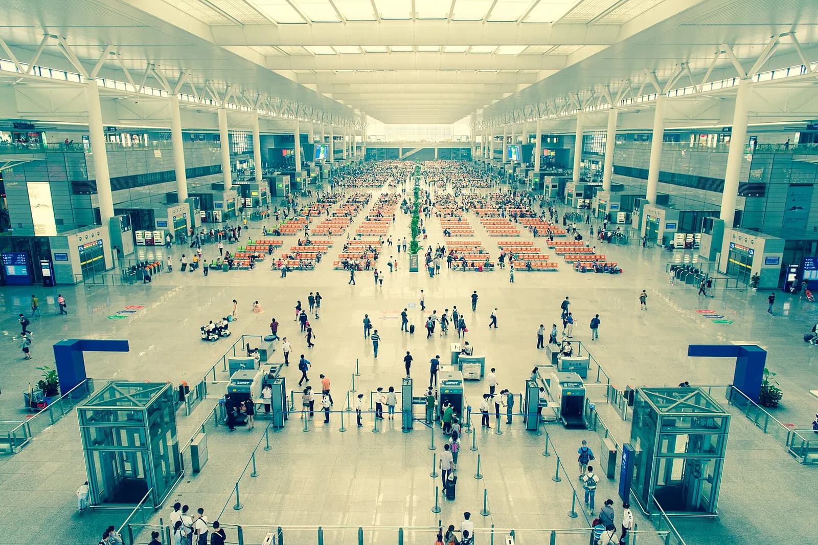 Travelers cross a vast, brightly lit concourse inside Shanghai Hongqiao Railway Station beneath high ceilings, escalators, and directional signage.