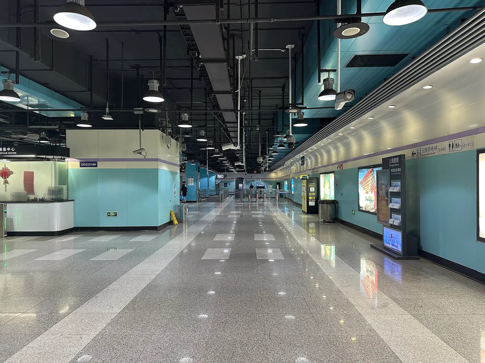 Passengers move through the ticket hall of Shanghai Metro's Hongqiao Airport Terminal 1 Station with gates, bilingual signs, and a wide underground concourse.