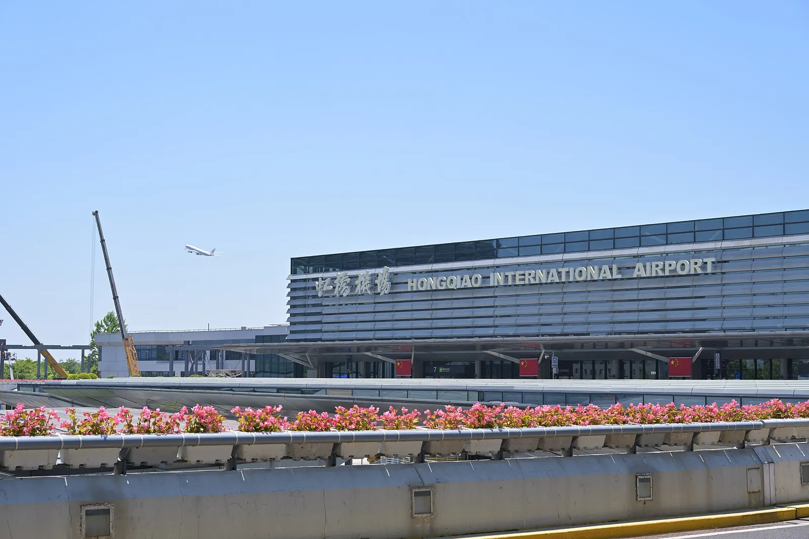 The exterior of Terminal 1 at Shanghai Hongqiao International Airport shows its smaller building, entrance roads, and landscaping in daylight.