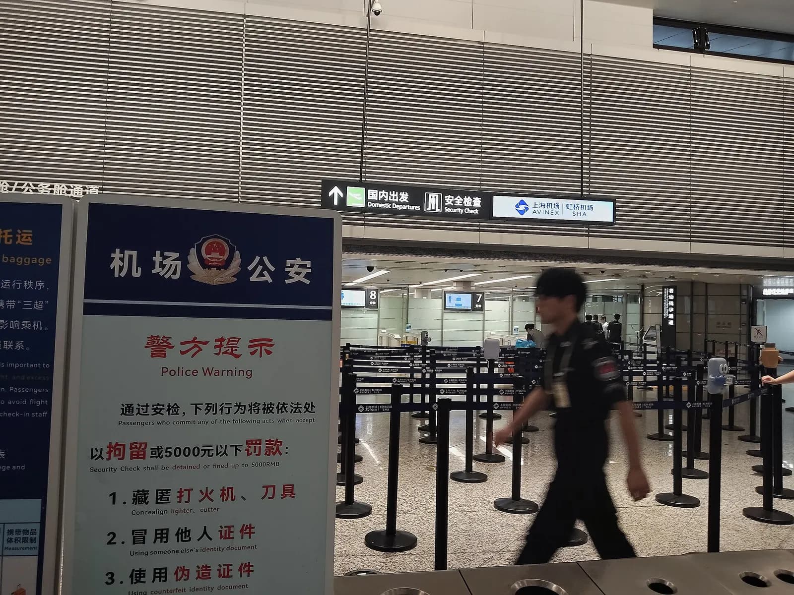 Queue lanes and stanchions lead to the domestic security screening entrance in Terminal 1, marked with bilingual airport signage.