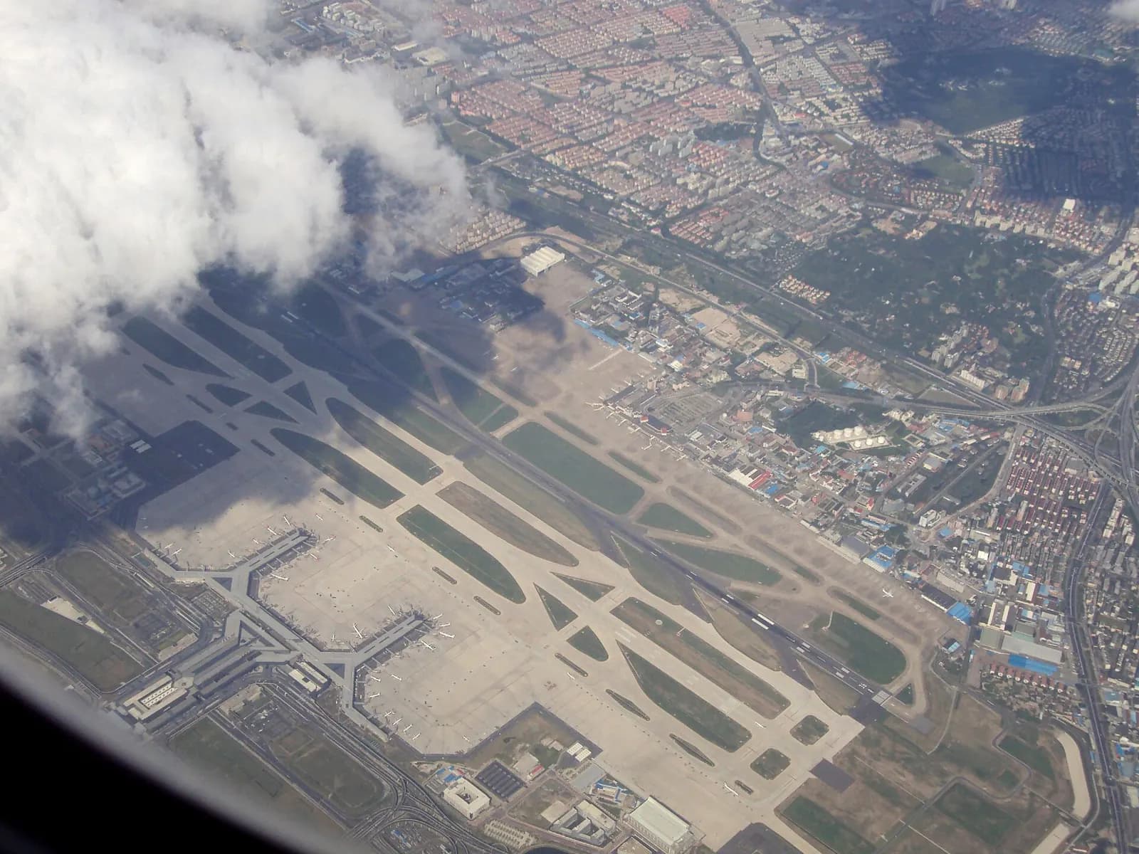 An aerial view from the southwest shows Hongqiao's large Terminal 2, the smaller Terminal 1, parallel runways, and the Hongqiao Railway Station beside the terminals.