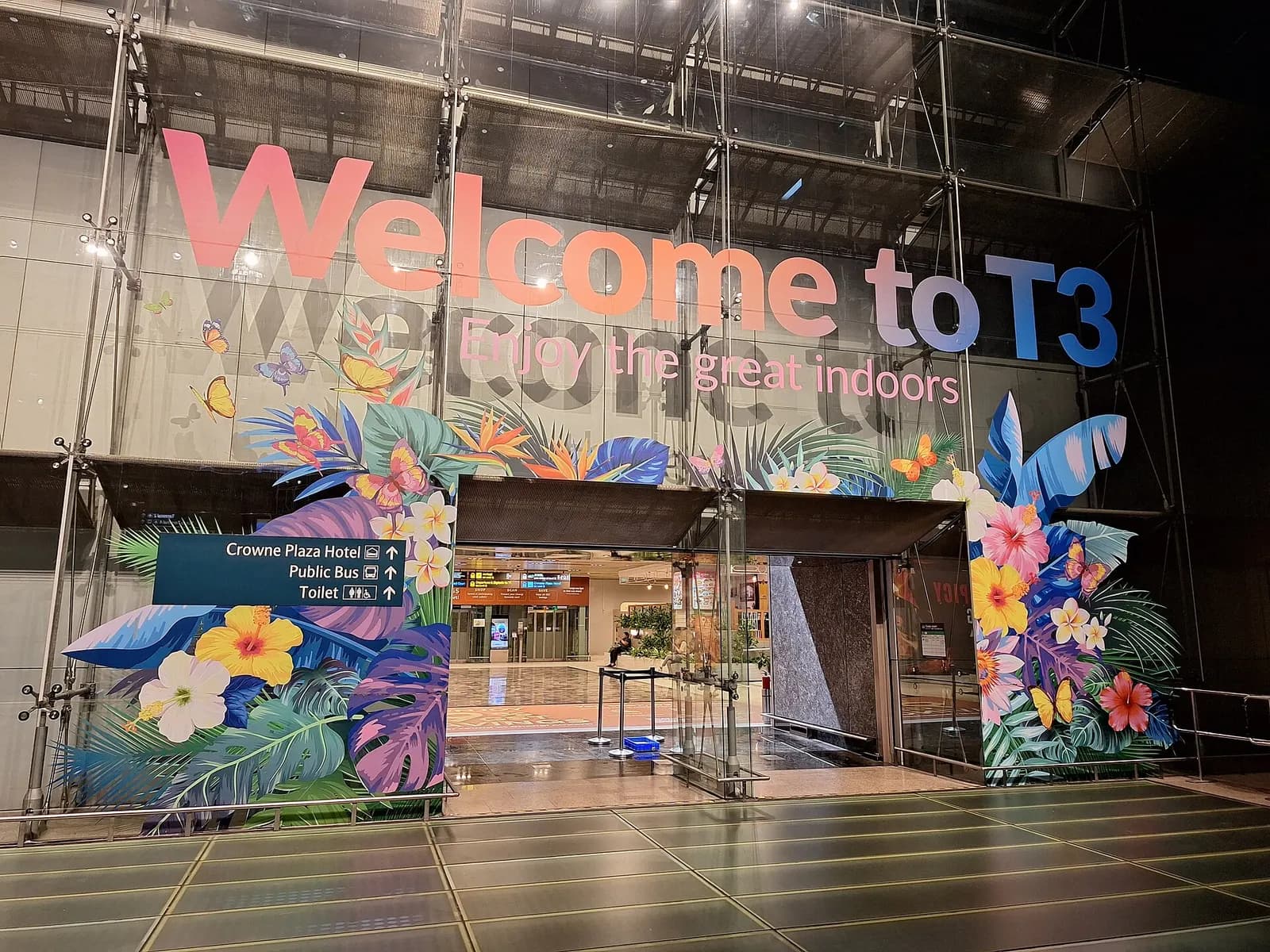 The glass-fronted entrance facade of Changi Airport Terminal 3 with drop-off roadway, signage, and landscaping in front.