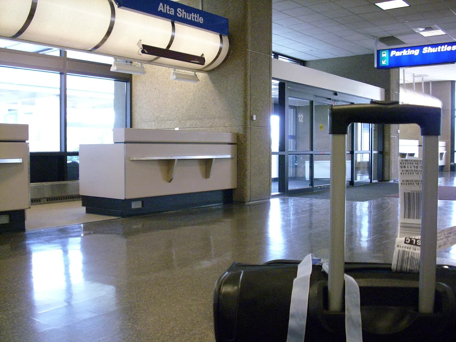 Baggage claim area with multiple carousels, tiled floors, and passengers waiting for luggage.