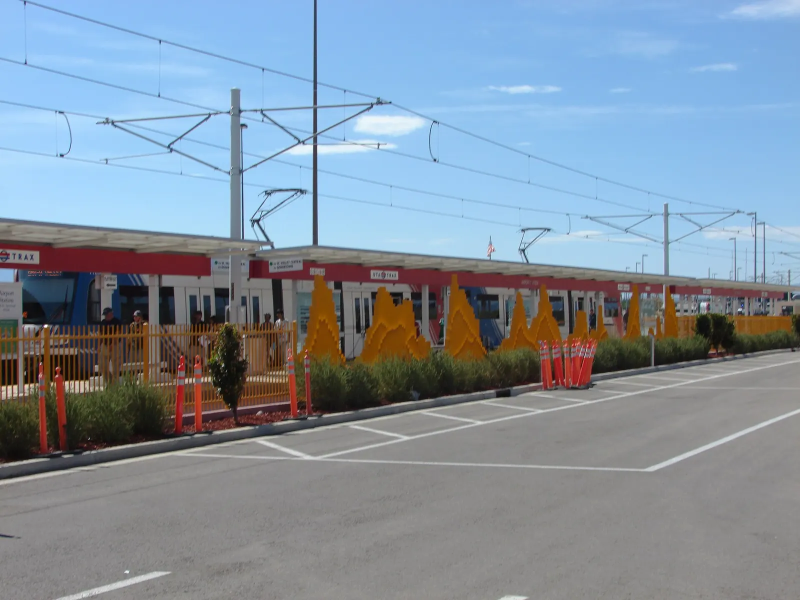 A UTA Green Line TRAX train at the airport station platform behind a decorative metal fence shaped like a mountain skyline.