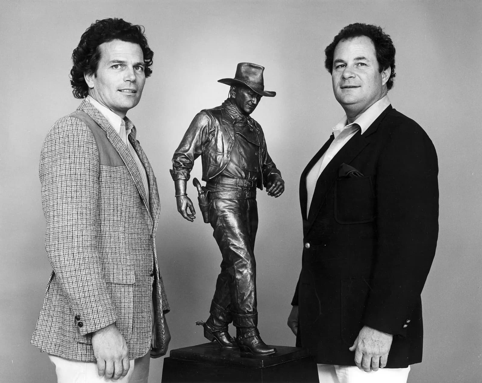 Patrick and Michael Wayne with a model of the proposed statue of their father, John Wayne. to be placed at John Wayne Airport, circa 1981. There are no known copyright restrictions on this image. All future uses of this photo should include the courtesy line, "Photo courtesy Orange County Archives."