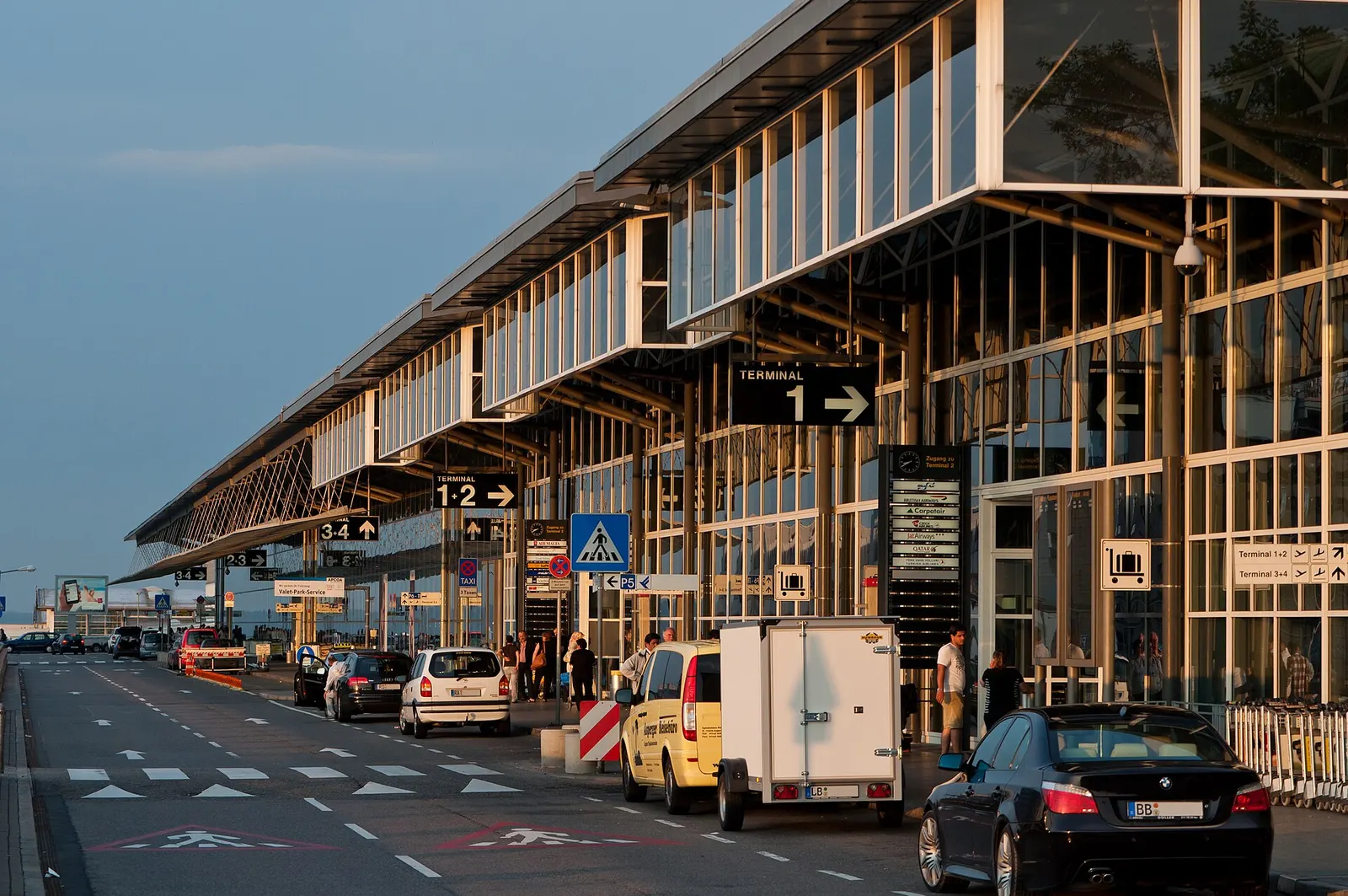 The traffic-side entrance to Terminals 1 through 4 at Stuttgart Airport with the terminal facades, roadway, and drop-off area.