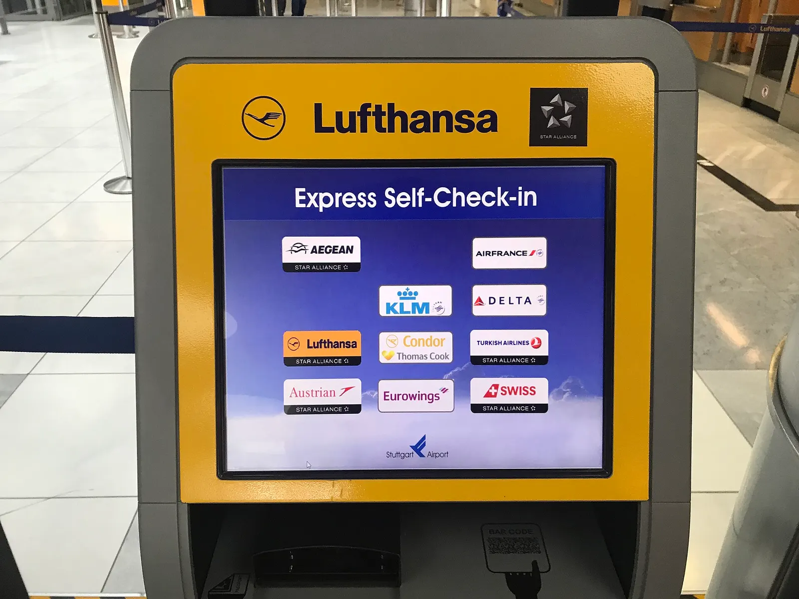 A Lufthansa check-in area in the Stuttgart Airport terminal with digital flight information screens above the counters.