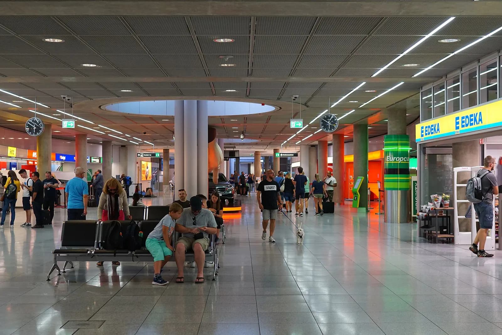 A bright, open interior concourse at Stuttgart Airport with passengers, shops, and multi-level walkways.