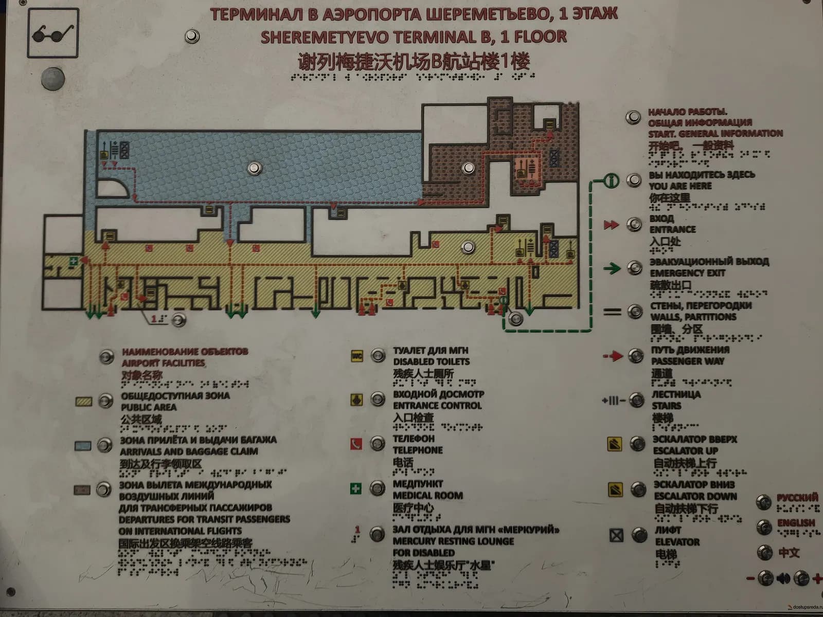 Close-up of multilingual wayfinding signage in Terminal B with Russian, English, and Chinese text plus Braille characters.