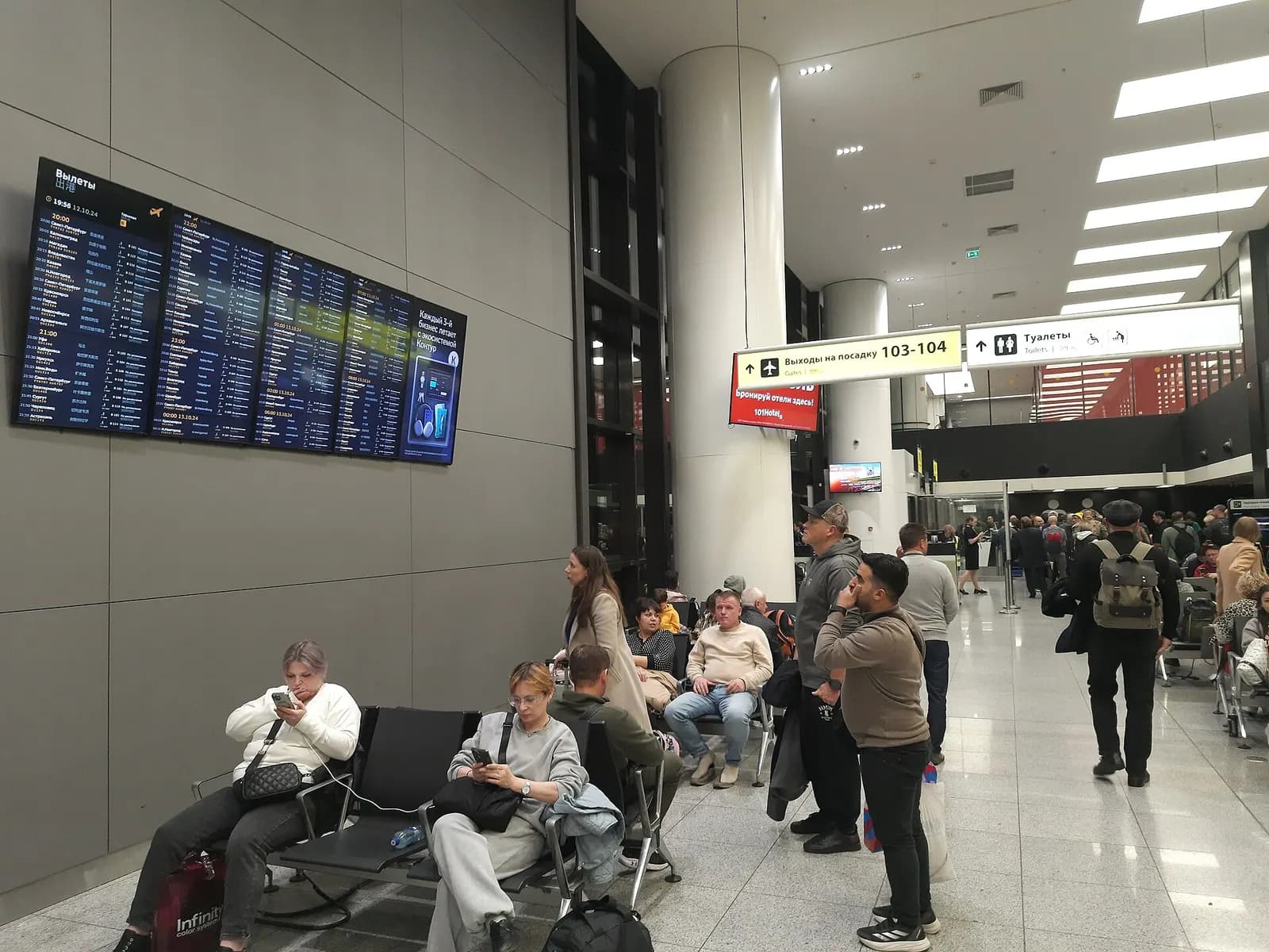 Spacious Terminal B departures concourse with high ceilings, moving walkways, seating areas, and passengers heading toward gates.