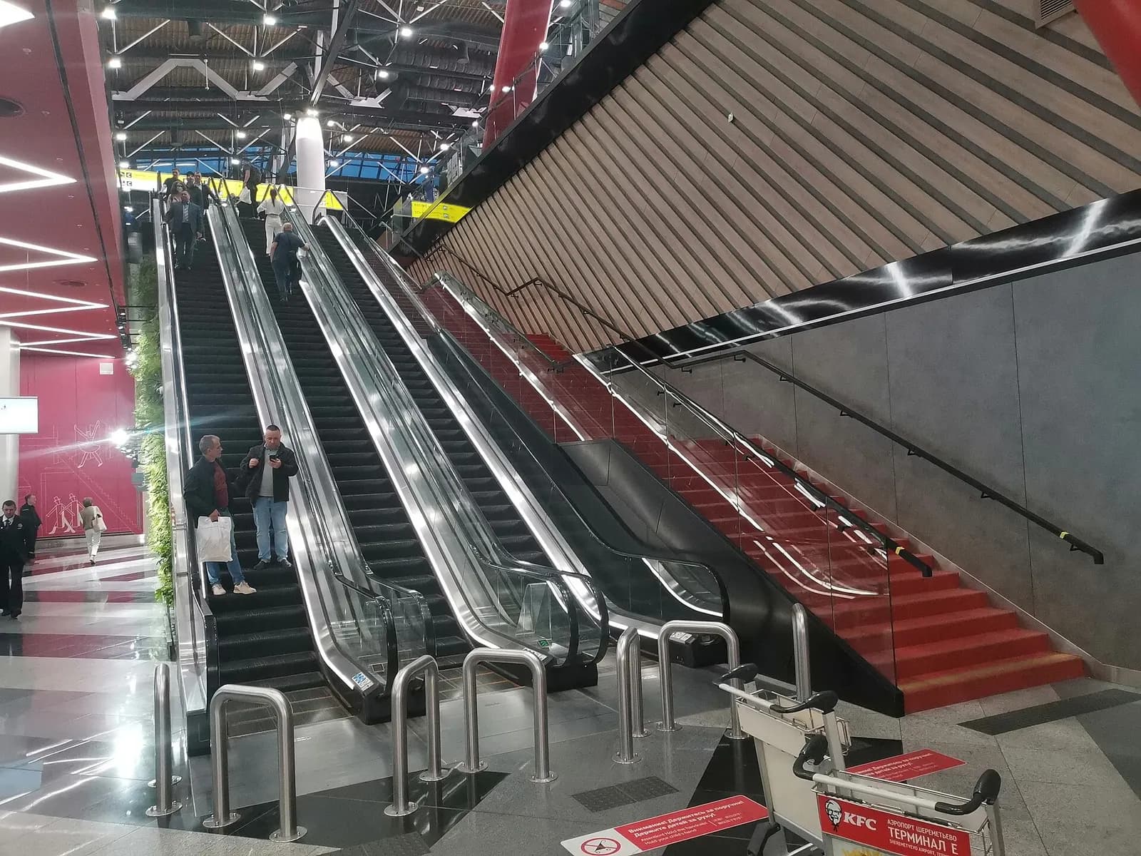 Bank of escalators inside Terminal C connecting floors, with glass balustrades and an open atrium visible beyond.