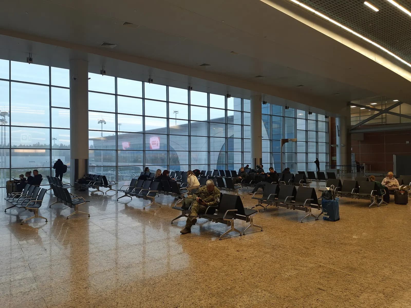 Airside waiting area in Terminal D with gate seating rows, flight information displays, and a wide polished concourse.