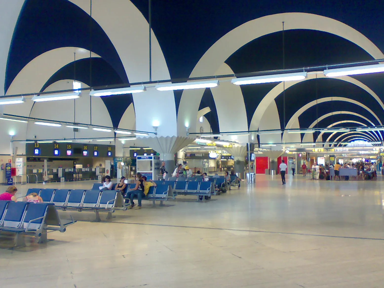 Departures façade of Seville Airport with passengers approaching the terminal entrance.