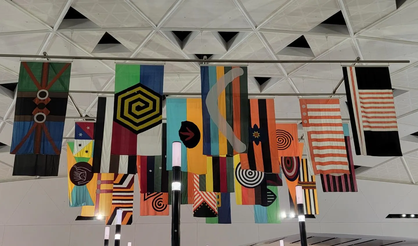 A public art installation displays rows of colorful Aboriginal and Torres Strait Islander flags inside Sydney Airport.