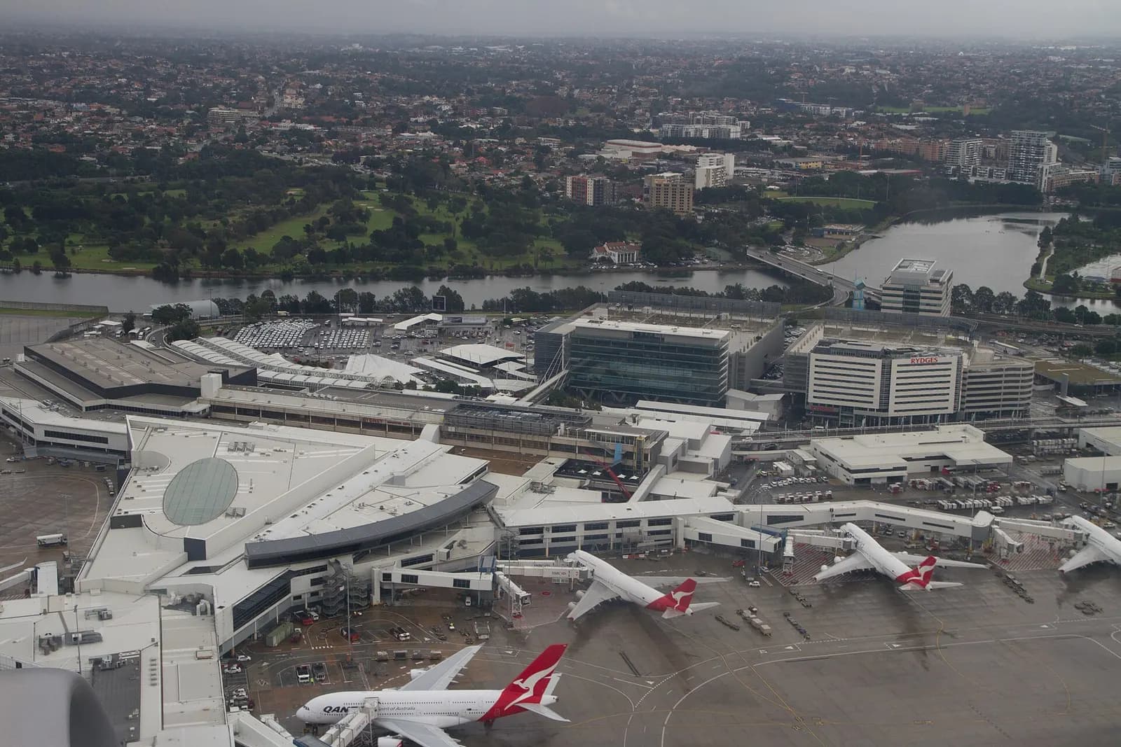 The curved glass-and-steel facade of Sydney Airport's International Terminal (T1) rises above the forecourt and access roads.