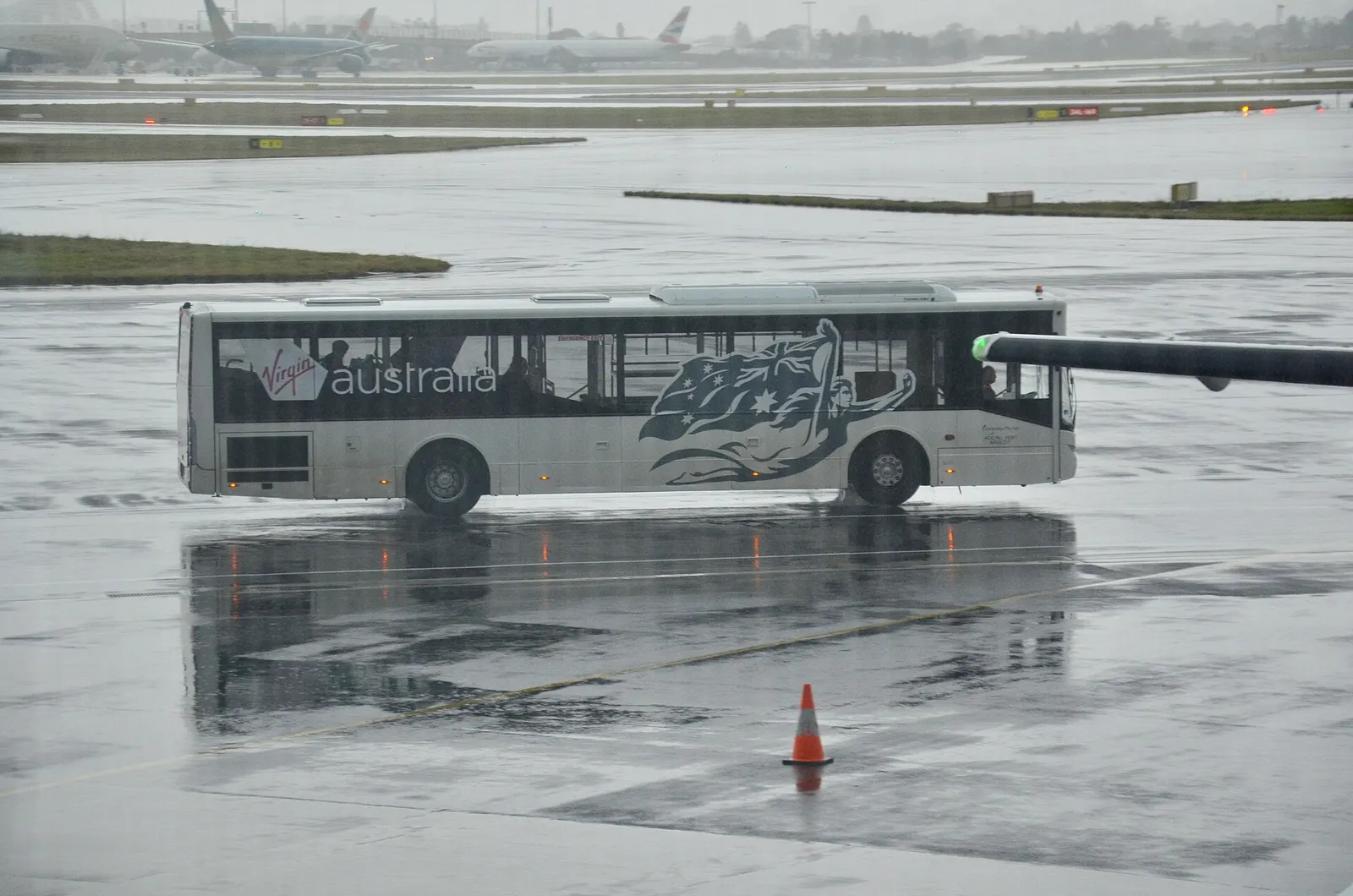 A Virgin Australia shuttle bus on the tarmac carries passengers between the terminal and a remote aircraft stand.