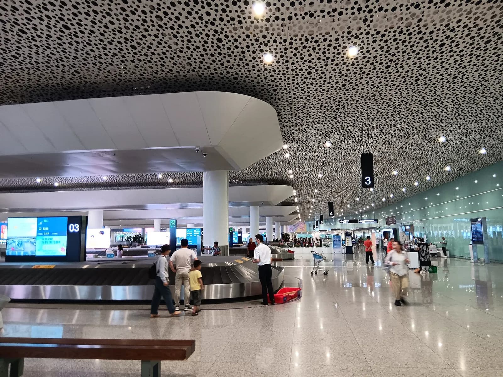 Baggage claim hall at Shenzhen Bao'an International Airport with multiple carousels, flight information displays, and arriving passengers.