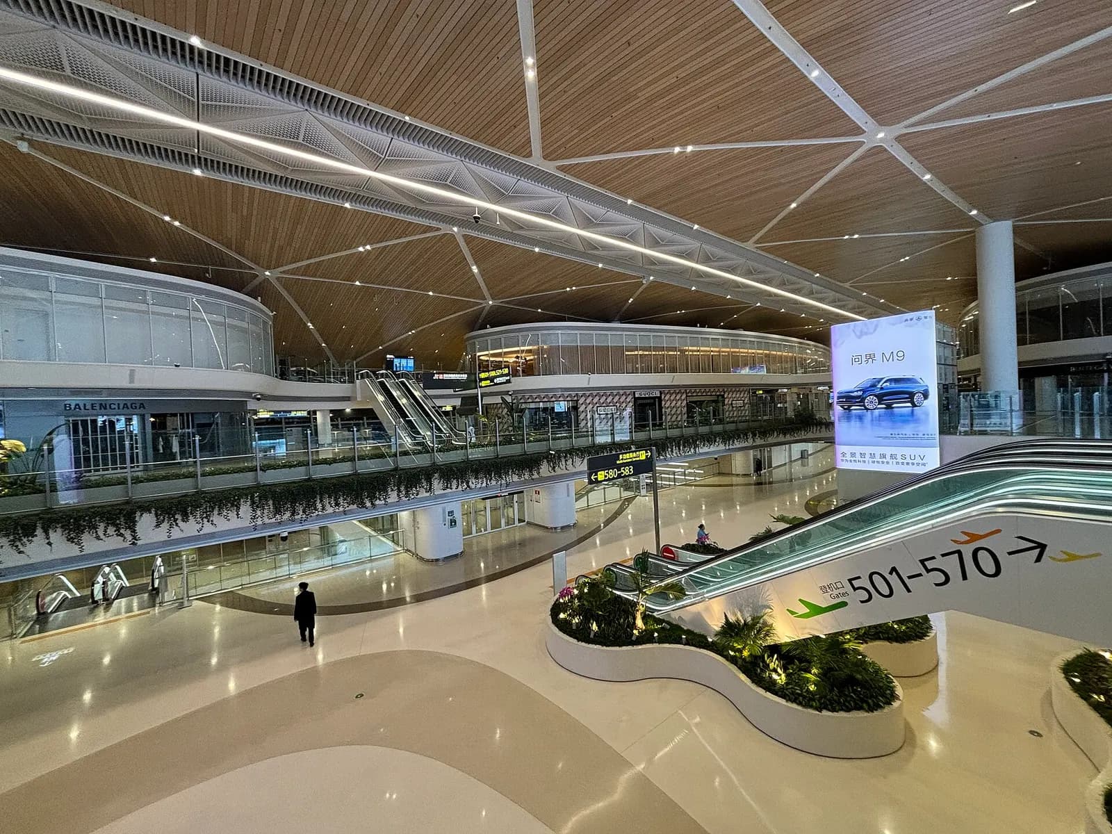 Central atrium of the Shenzhen airport satellite terminal with multi-level walkways, shops, and gate corridors branching off both sides.