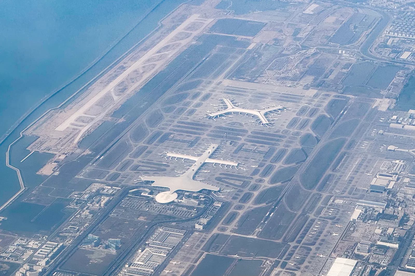 Aerial view of Shenzhen Bao'an International Airport showing the curved Terminal 3 main building, satellite concourses, and surrounding runways and taxiways.