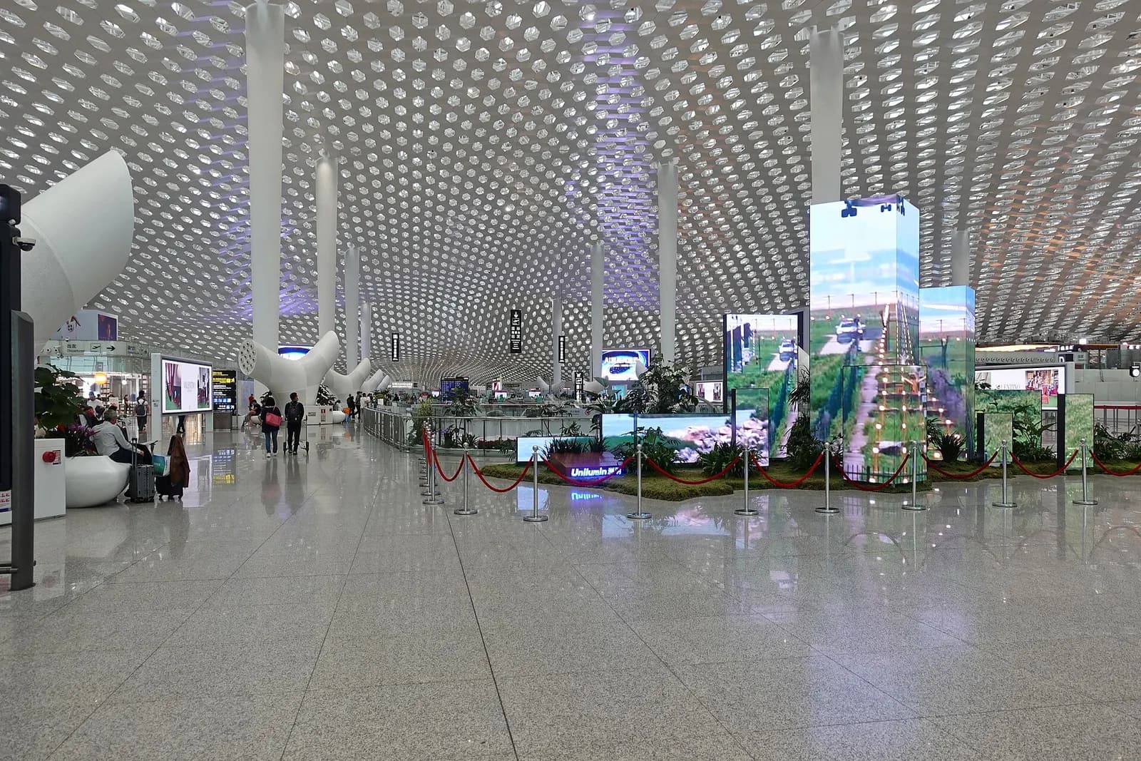 Bright, spacious departure hall inside Shenzhen Bao'an International Airport Terminal 3 with check-in counters, departure boards, and travelers with luggage.
