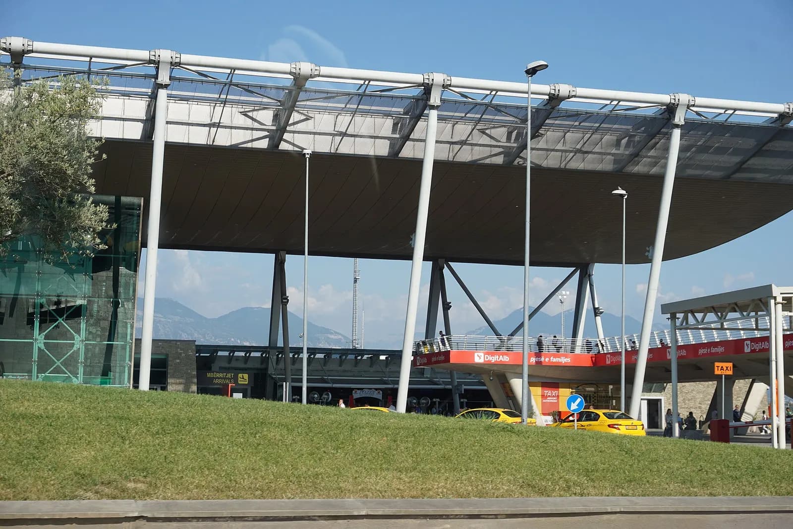 Arrivals frontage at Tirana International Airport with Mbërritjet / Arrivals signage and yellow taxis