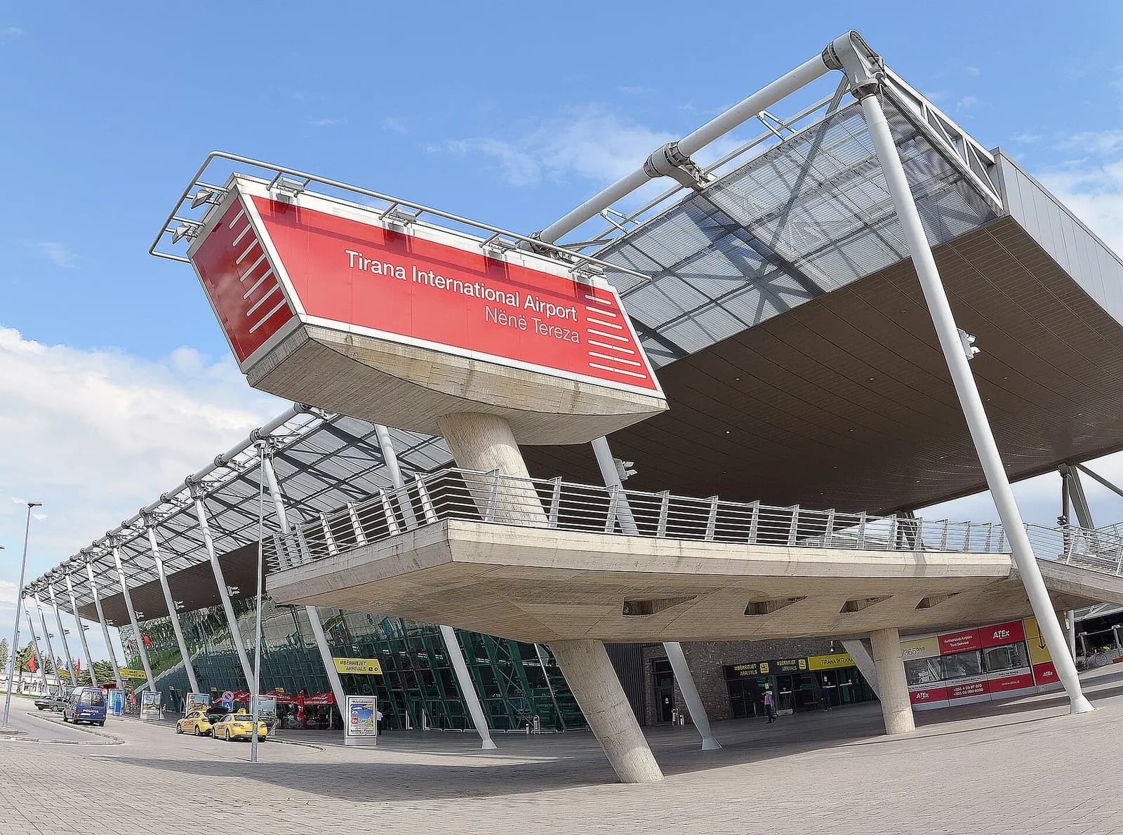 Tirana International Airport Nënë Tereza terminal exterior with the red airport name sign and yellow taxis at arrivals