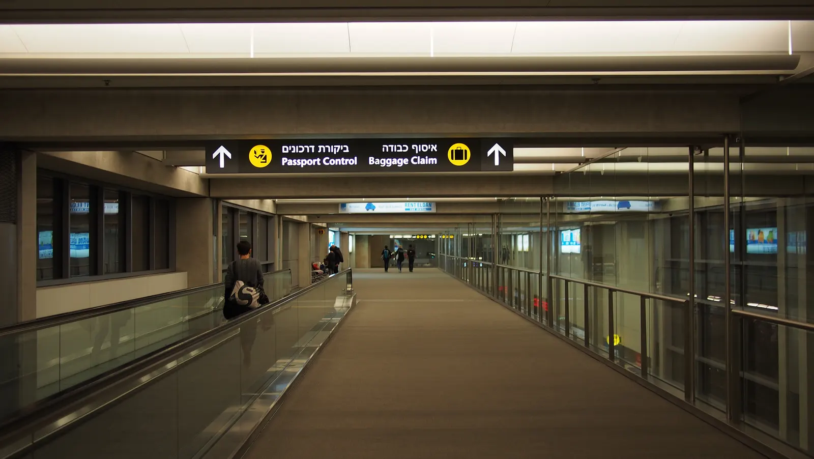 Passengers riding a moving sidewalk through a spacious, modern corridor inside Ben Gurion Airport.