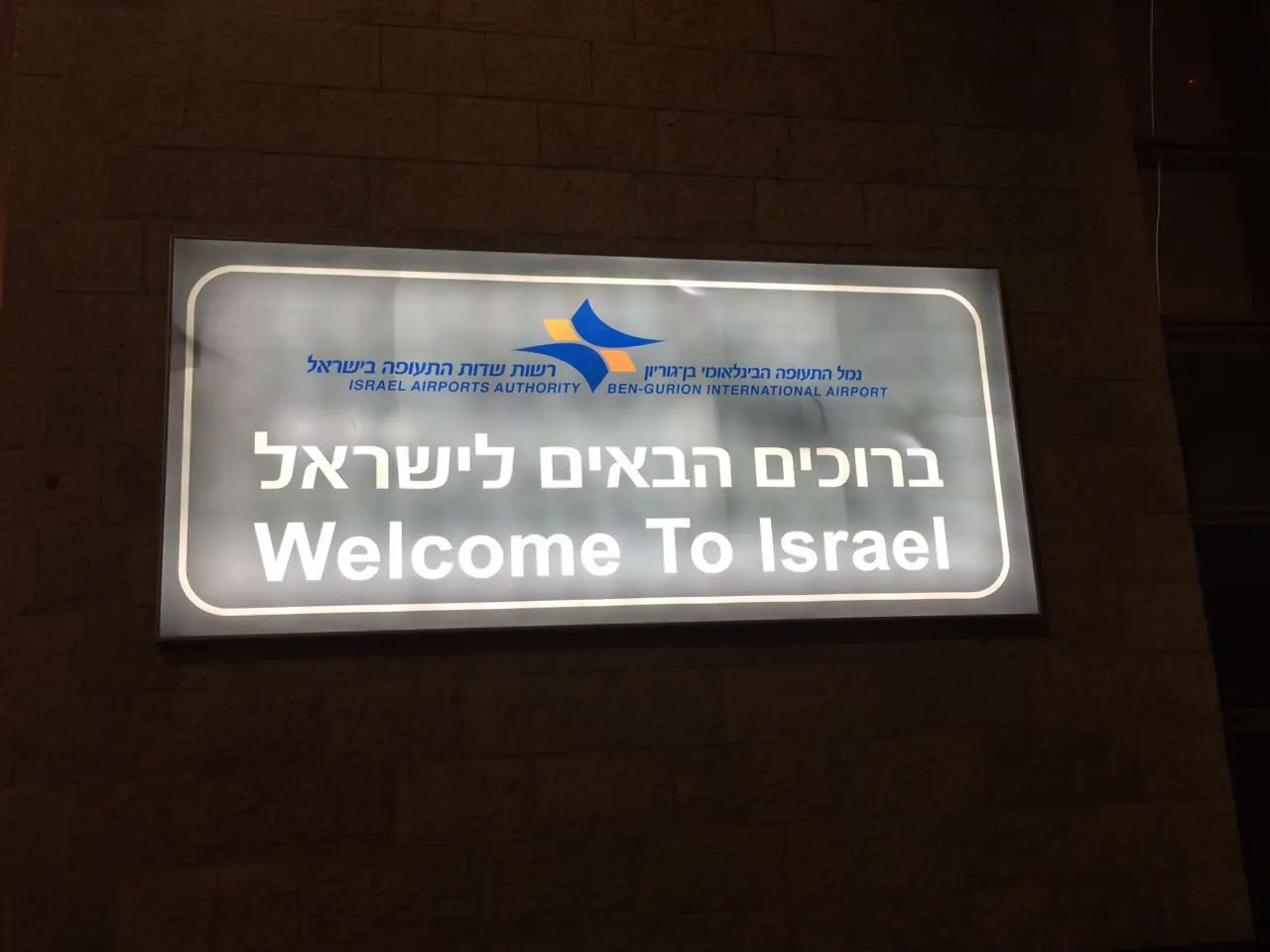 A large illuminated "Welcome to Israel" sign in English and Hebrew mounted in the arrivals area of Ben Gurion Airport.