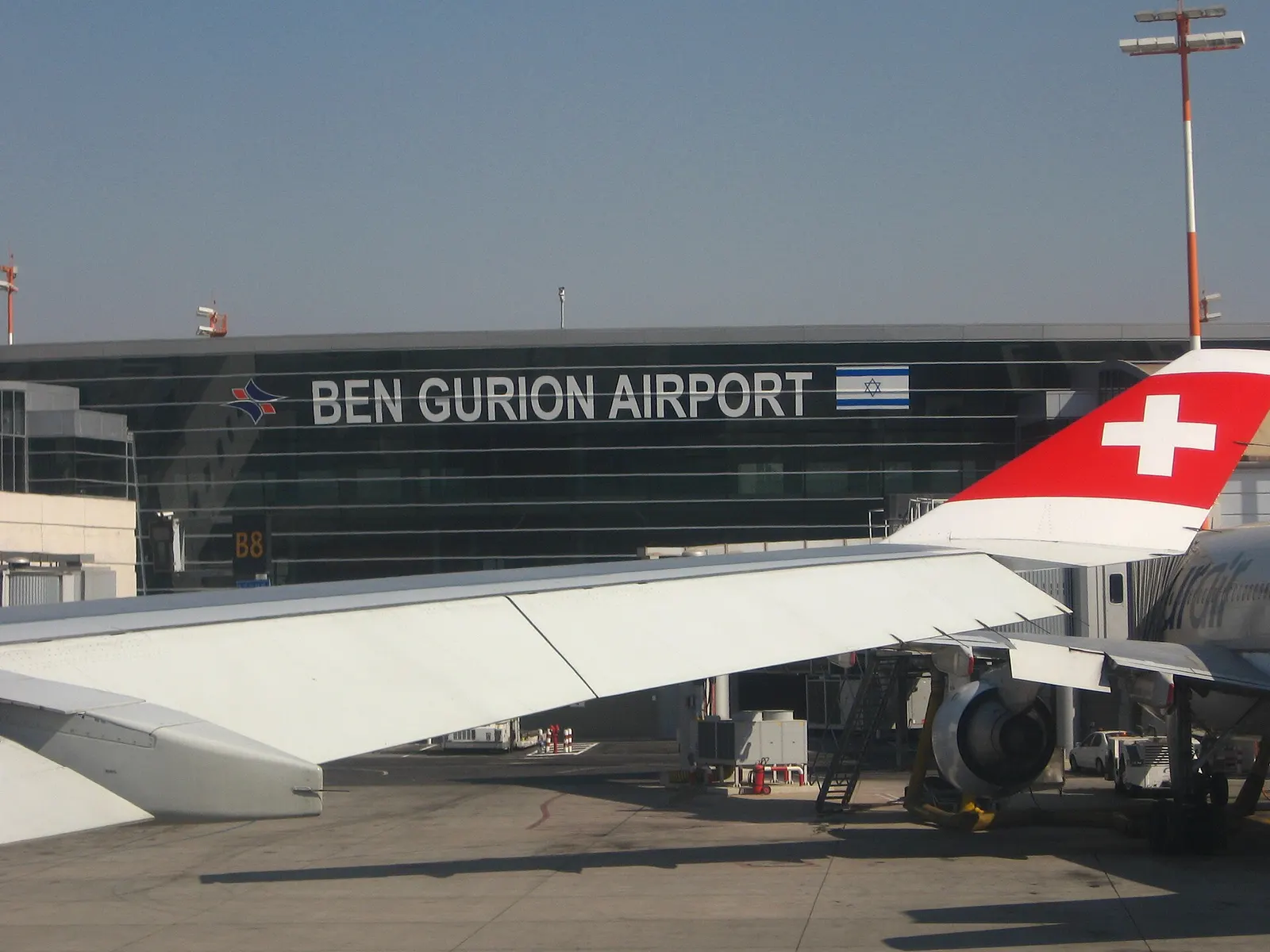 The main Terminal 3 building of Ben Gurion International Airport viewed from the tarmac, showing its sweeping curved roofline and glass facade.