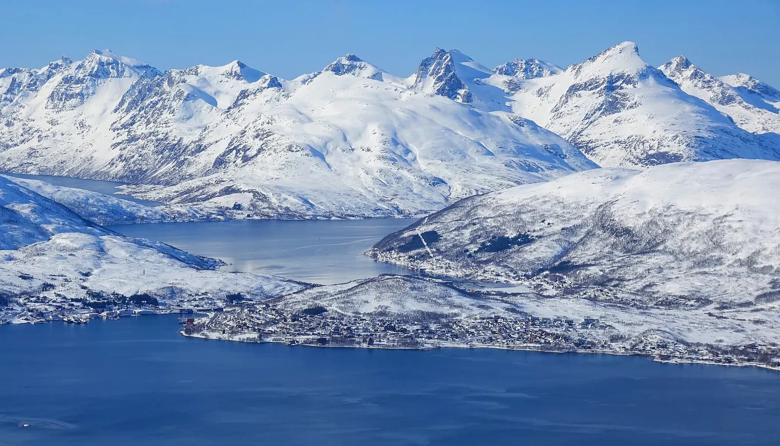 The photo shows Eidkjosen, a residential area in Tromsø municipality. The photo was taken from a commercial flight just after take-off from Tromsø airport. We see Eidkjosen from the east, with several mountains located on the same island in the background; Buren, Hollendaren, Store Blåmannen and Mid
